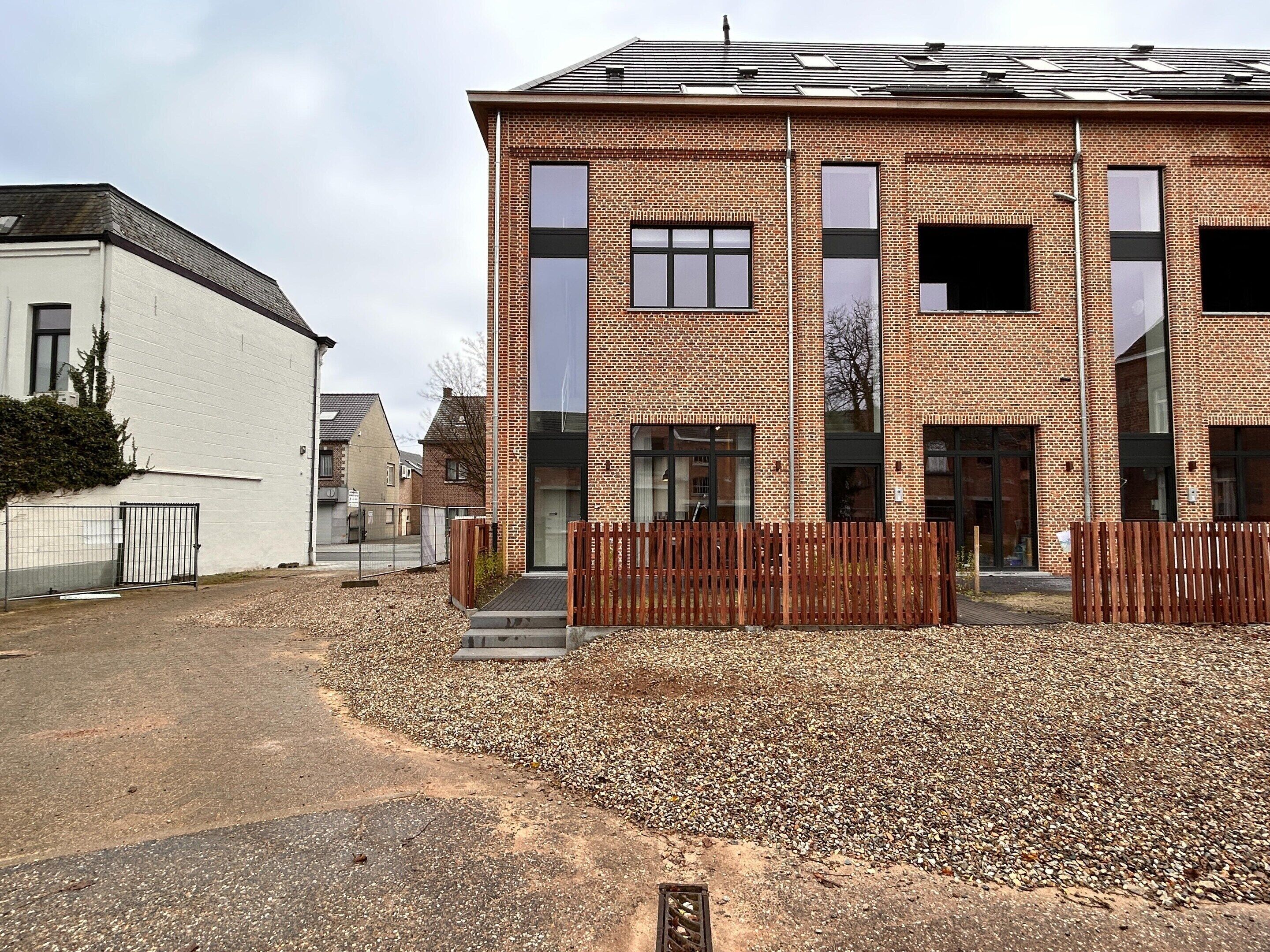 A modern building with a brick facade, large windows, and a gravel driveway.