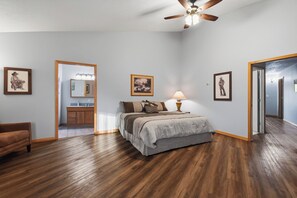 Une chambre à coucher avec un lit, un ventilateur de plafond, un plancher en bois et des tableaux encadrés accrochés aux murs.