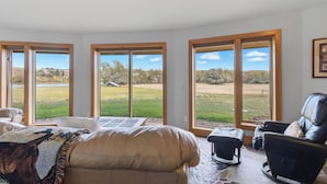 Amplia habitación con ventanas grandes que dan a un campo cubierto de hierba y árboles. Hay un sofá de cuero y una butaca de cuero negro.