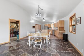 Une cuisine spacieuse avec des meubles en bois et un îlot central, un coin repas doté d’un sol carrelé en pierre et un lustre.