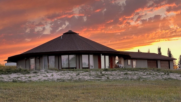 Un edificio de una sola planta con techo plano y ventanas amplias, ubicado en un campo cubierto de césped, con un cielo al atardecer de fondo.