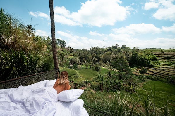 A person lying in bed with a view of a lush green landscape and terraced fields. - Camaya Bali (Selat)