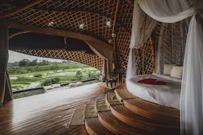 A room with a bed, a chair, and a view of a green landscape. - Camaya Bali (Selat)