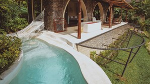 A poolside area with a stone structure, a hammock, and a lounge area with a view of the pool. - Camaya Bali (Selat)