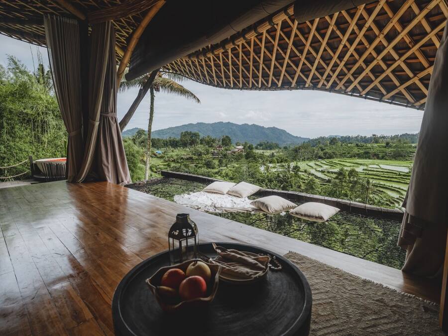 A wooden table with a fruit bowl, a lantern, and a view of terraced fields and mountains.