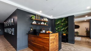 A reception area with a wooden reception desk, a wall-mounted shelf with trophies and decorative items, and a green wall with a vertical garden. - Spacious 3BR Loft | 15 From NYC & MetLife| Great Value | Groups Welcome (Jersey City)