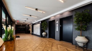 A modern hotel lobby with a geometric patterned floor, dark walls, and a large potted plant. - Spacious 3BR Loft | 15 From NYC & MetLife| Great Value | Groups Welcome (Jersey City)