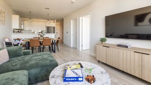 A modern apartment with a dining area, kitchen, living room, and a large TV. - Spacious 3BR Loft | 15 From NYC & MetLife| Great Value | Groups Welcome (Jersey City)