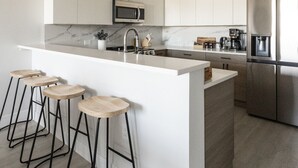 A modern kitchen with a central island, bar stools, stainless steel appliances, and pendant lighting. - Spacious 3BR Loft | 15 From NYC & MetLife| Great Value | Groups Welcome (Jersey City)