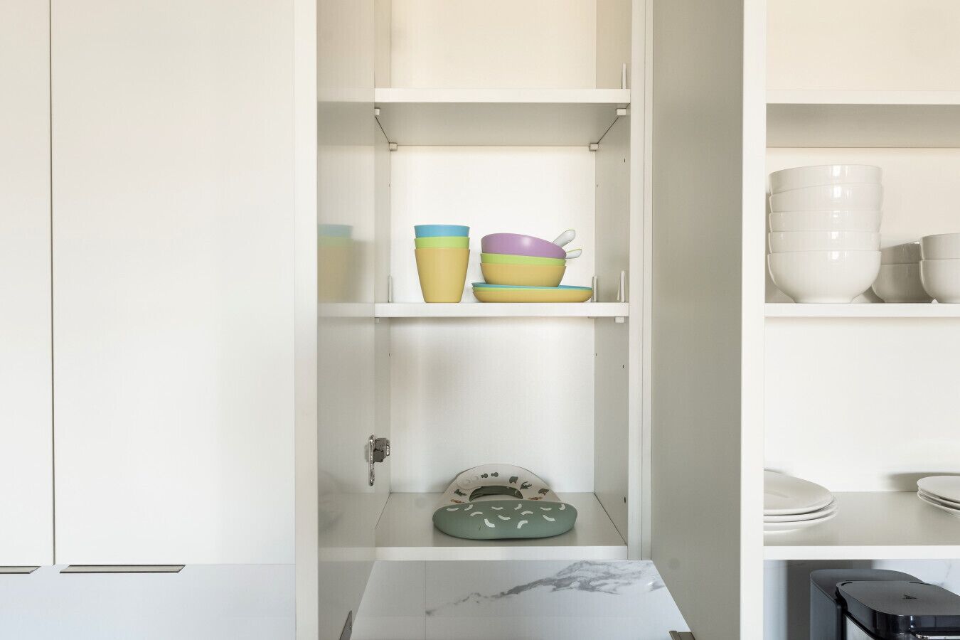 Una cocina con armarios blancos, encimera de mármol y utensilios de cocina de colores en estantes.