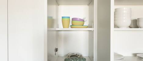 Una cocina con armarios blancos, encimera de mármol y utensilios de cocina de colores en estantes.
