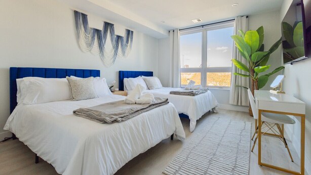 Una habitación de hotel moderna con dos camas, un ventanal grande y un escritorio con espejo.