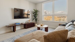 Una sala de estar moderna con una televisión de pantalla plana, una planta en maceta, una mesa de centro redonda y un sofá con cojines a rayas.