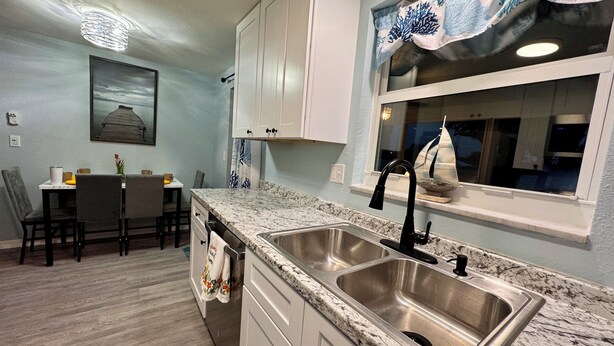 A kitchen with granite countertops, stainless steel sink, and white cabinets.