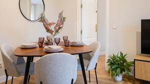 Un comedor con una mesa redonda, dos sillas grises, un florero con hojas decorativas y una planta en maceta.