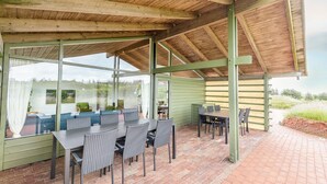 A covered outdoor dining area with a table and chairs, a brick floor, and a view of the surrounding landscape. - Vigso Feriecenter in Hanstholm (Hanstholm)