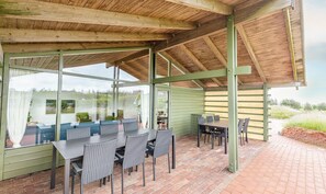 A covered outdoor dining area with a table and chairs, a brick floor, and a view of the surrounding landscape. - Vigso Feriecenter in Hanstholm (Hanstholm)