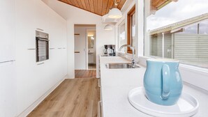 A modern kitchen with white cabinetry, a wooden floor, a built-in oven, a sink, and a window with blinds. - Vigso Feriecenter in Hanstholm (Hanstholm)