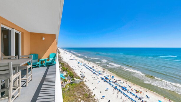 Ein Balkon mit Blick auf einen Strand, ein Schwimmbad und einen strahlend blauen Himmel.