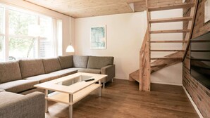 Een moderne woonkamer met een houten trap, een bank, een salontafel en een schilderij aan de muur.