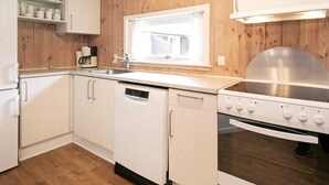 Een keuken met houten lambrisering, witte kasten, een roestvrijstalen spoelbak en een ingebouwde oven.