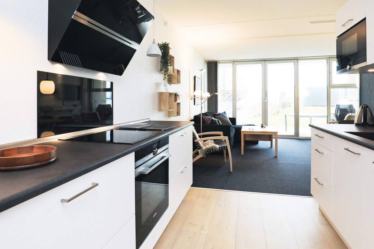 A modern kitchen with a black stove, white cabinets, and a large window offering a view of the outdoors.