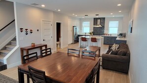 A modern kitchen with a central island, a dining area with a wooden table and chairs, and a living room with a sofa. - Furnished 3BR Townhome with Mountain View and Minutes from Downtown & Stadiums (Denver)