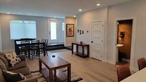 A living room with a sofa, coffee table, and dining area with chairs. There is a door leading to another room and a small table with a plant. - Furnished 3BR Townhome with Mountain View and Minutes from Downtown & Stadiums (Denver)