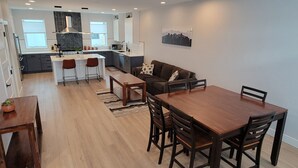 A modern kitchen with white cabinets, a central island, and a dining area with a wooden table and chairs. - Furnished 3BR Townhome with Mountain View and Minutes from Downtown & Stadiums (Denver)