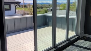 A room with large sliding glass doors leading to a balcony with a view of a residential area and a clear sky. - Furnished 3BR Townhome with Mountain View and Minutes from Downtown & Stadiums (Denver)