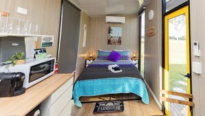 Een kleine kamer met een bed, nachtkastjes, een magnetron, een plantje en uitzicht op de omgeving.