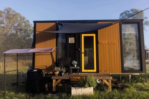 Une petite cabane en bois avec une porte coulissante, un patio avec une table et des chaises, et une pancarte indiquant « Jucyando Cottage ».