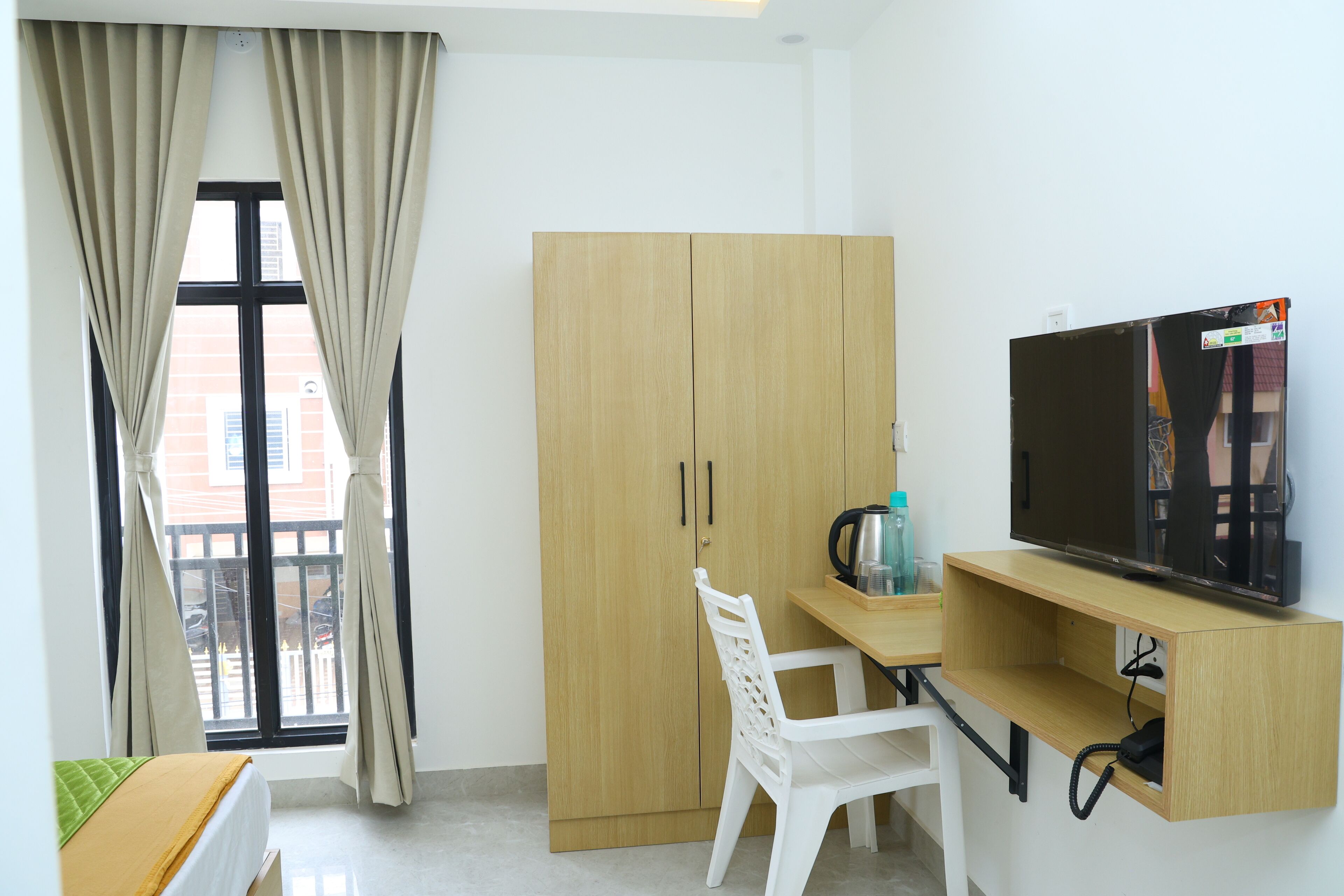 A compact room with a bed, a desk with a TV, a wardrobe, and a window with curtains.