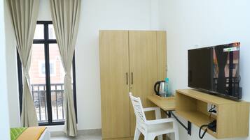 A compact room with a bed, a desk with a TV, a wardrobe, and a window with curtains.
