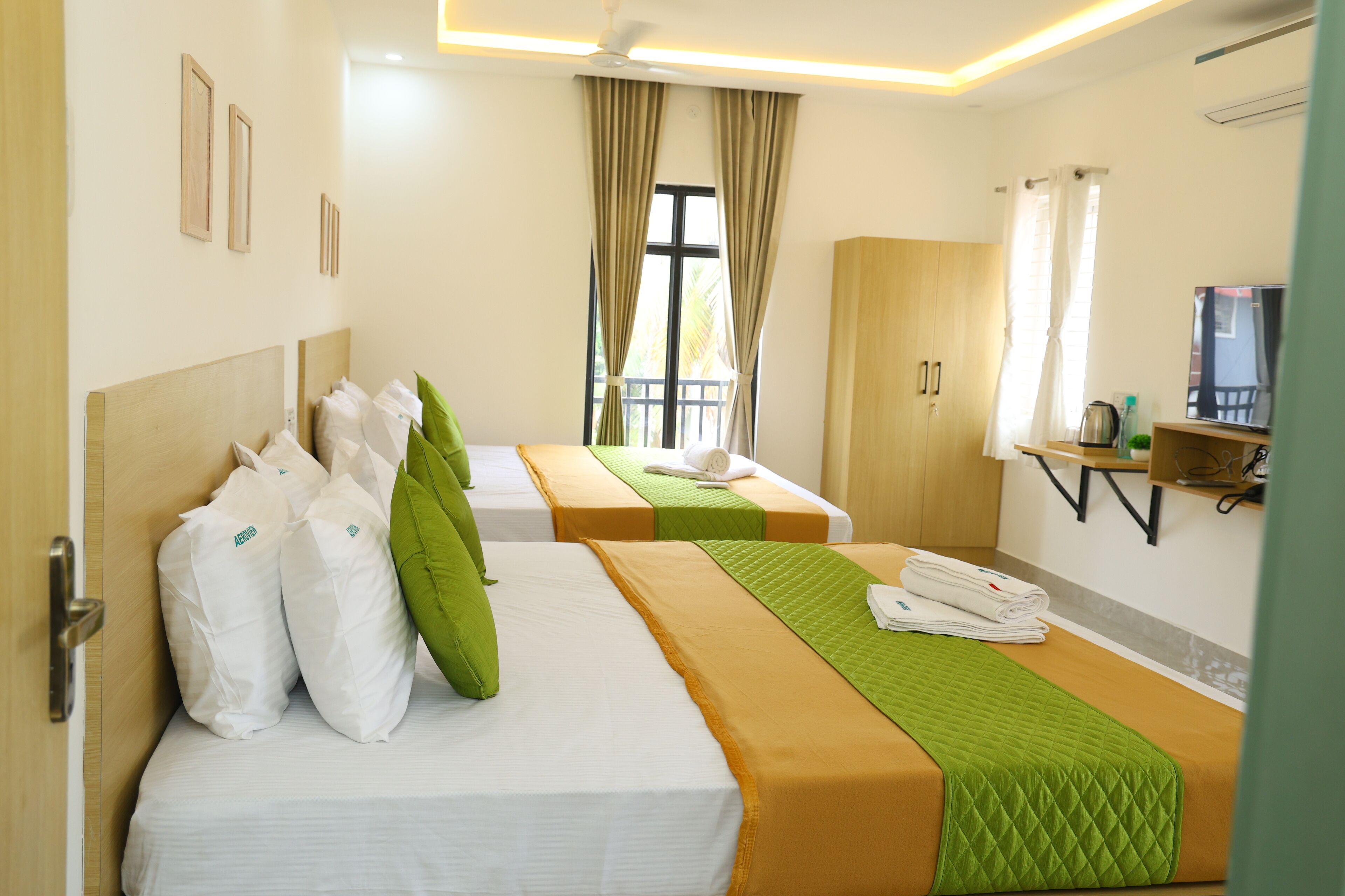 A hotel room with two beds, a wardrobe, a TV, and a window with curtains.