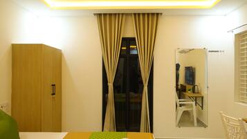 A bedroom with a bed, a wardrobe, a desk with a chair, a mirror, and a window with curtains.