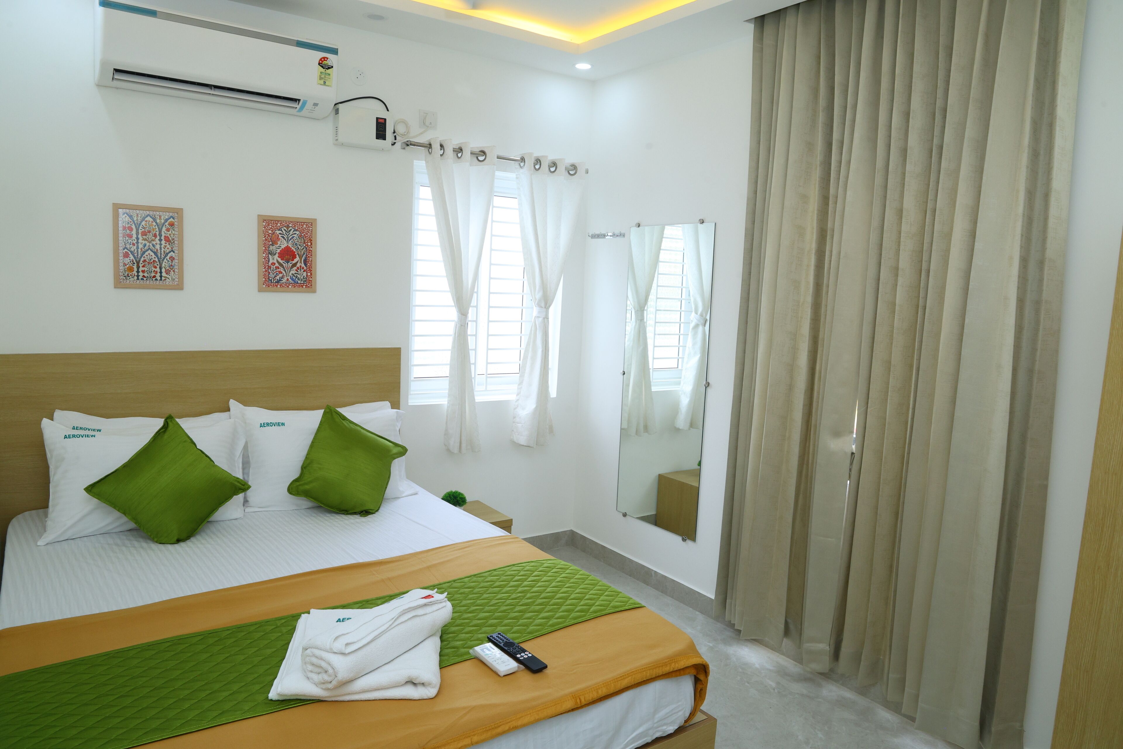 A hotel room with a bed, green pillows, a green quilt, a remote control, and a mirror.