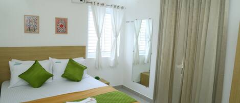 A hotel room with a bed, green pillows, a green quilt, a remote control, and a mirror.