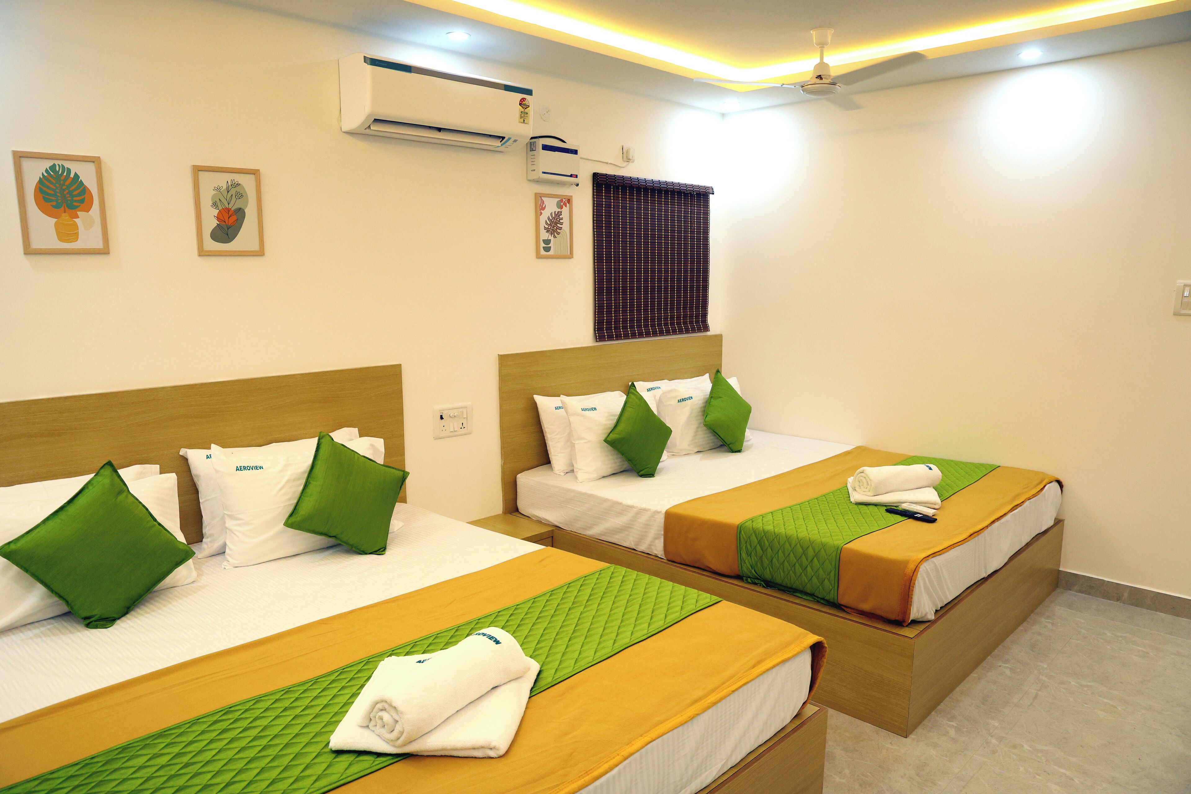 Habitación de hotel con dos camas, cada una con ropa de cama y almohadas verdes, un cabecero de madera y una colcha verde acolchada.