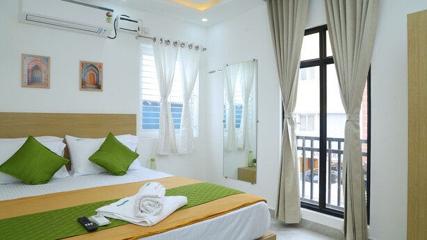 A hotel room with a bed, green pillows, a green bedspread, a mirror, a window with curtains, and a view of the outside. - Aeroview Homestay Chennai Airport (Chennai)