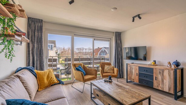 A modern living room with a sofa, two armchairs, a coffee table, a TV, and a wooden cabinet. - Comfortable and Modern Furnished 4-person Apartment (De Koog)
