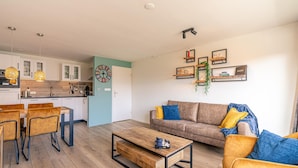 A modern living room with a wooden coffee table, a sofa, and a dining area with chairs. - Comfortable and Modern Furnished 4-person Apartment (De Koog)