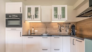 A modern kitchen with white cabinets, a built-in oven, and a wooden backsplash. - Comfortable and Modern Furnished 4-person Apartment (De Koog)
