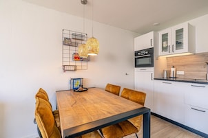 A modern kitchen with white cabinets, a black oven, and a wooden dining table with six chairs.