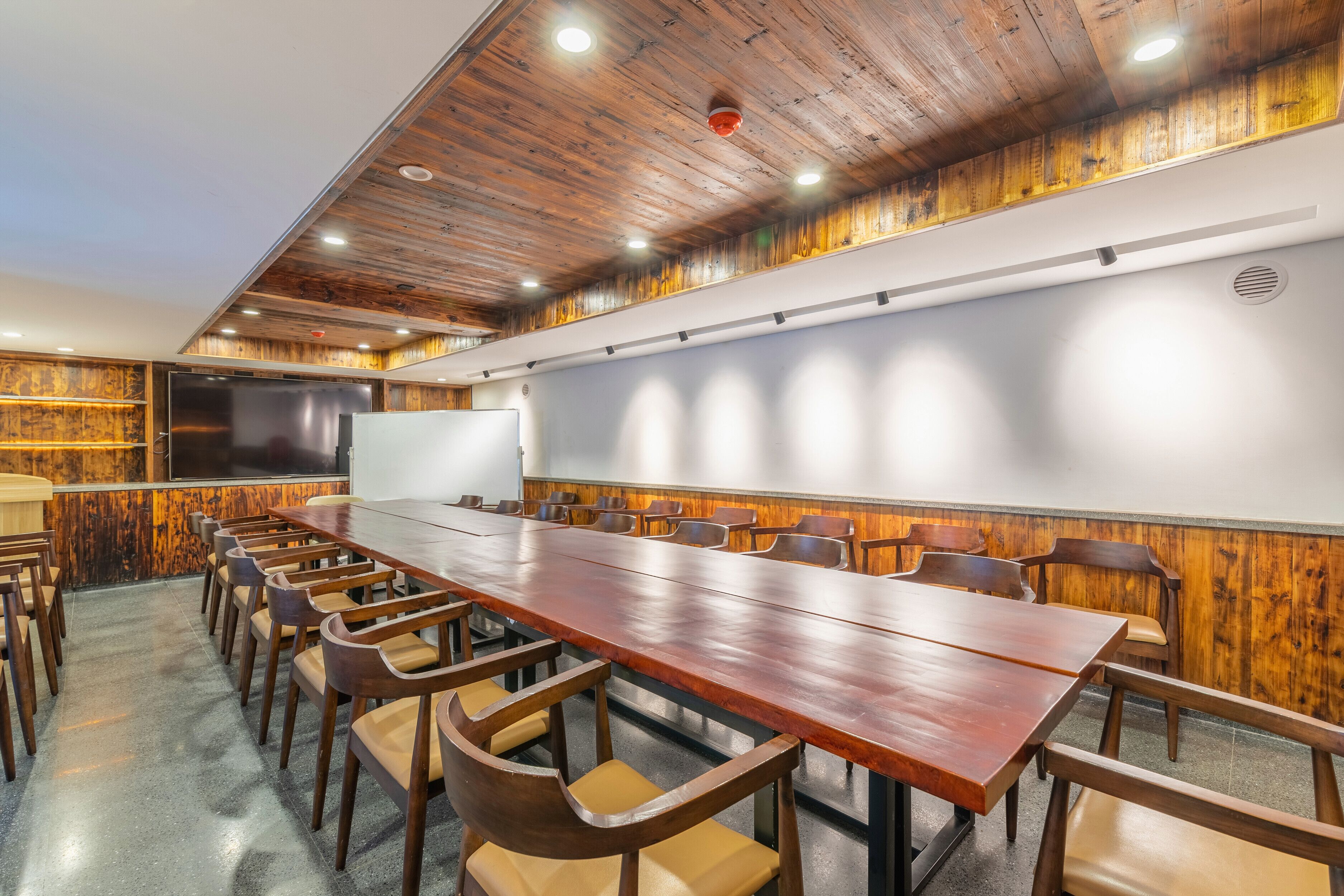 A conference room with a long wooden table, multiple chairs, a whiteboard, and a projector screen.