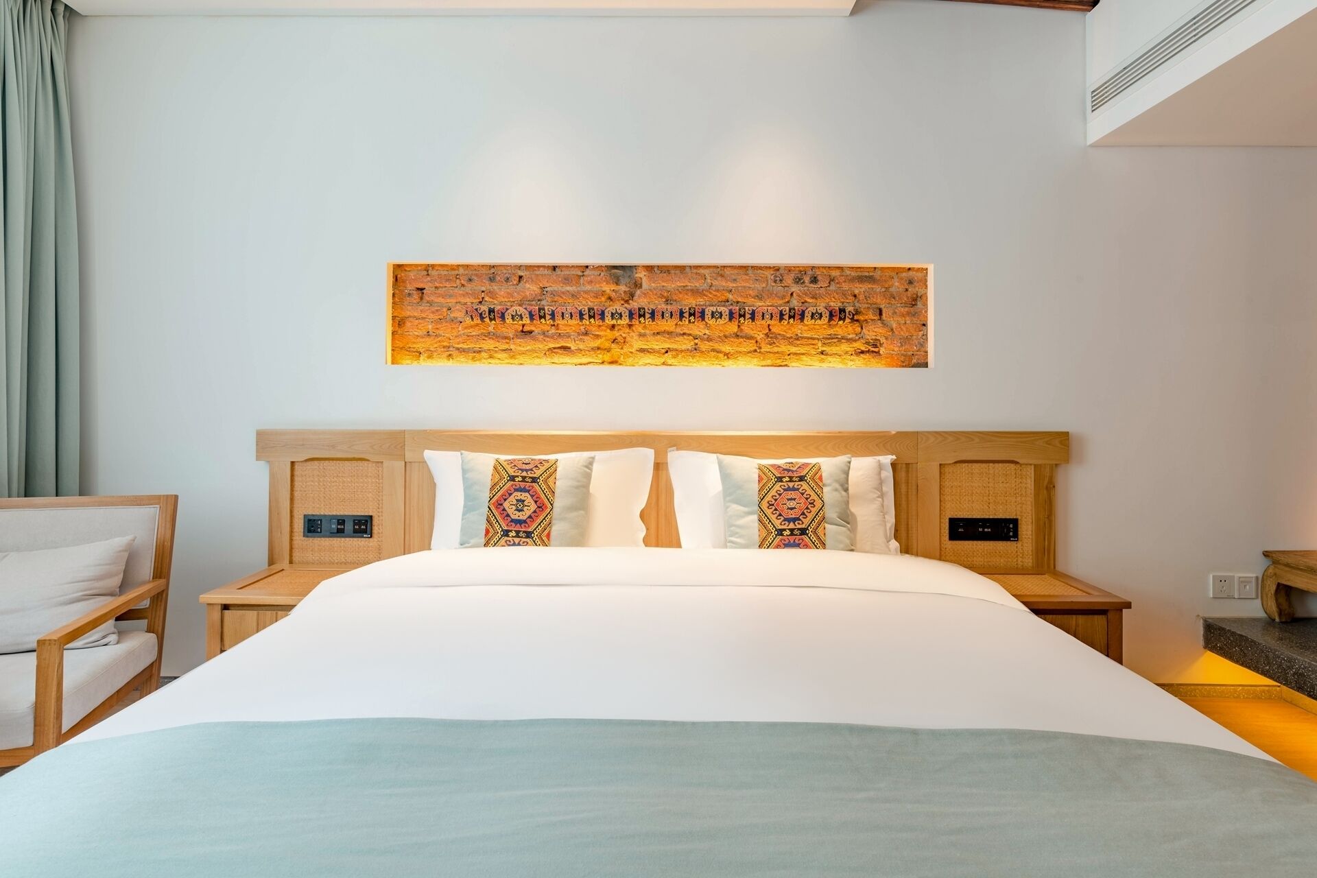 A hotel room with a large bed, two bedside tables, a headboard with a decorative panel, and a wall-mounted artwork.
