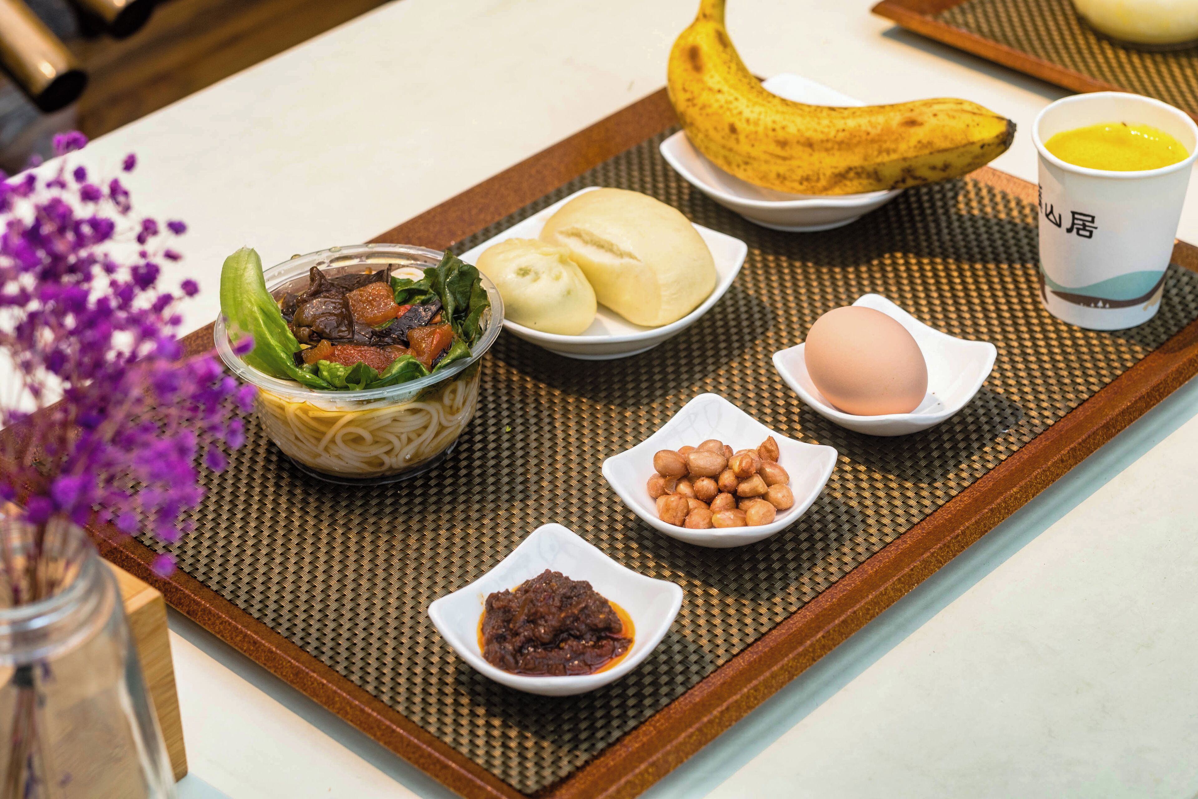 Una bandeja con alimentos que incluyen un plátano, dumplings, una ensalada, cacahuates, un huevo y un recipiente pequeño con salsa.