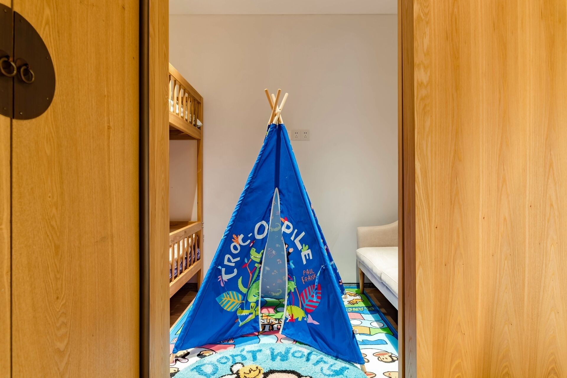 Um quarto com uma estrutura em forma de tenda azul no chão, uma estante de livros e uma cama.