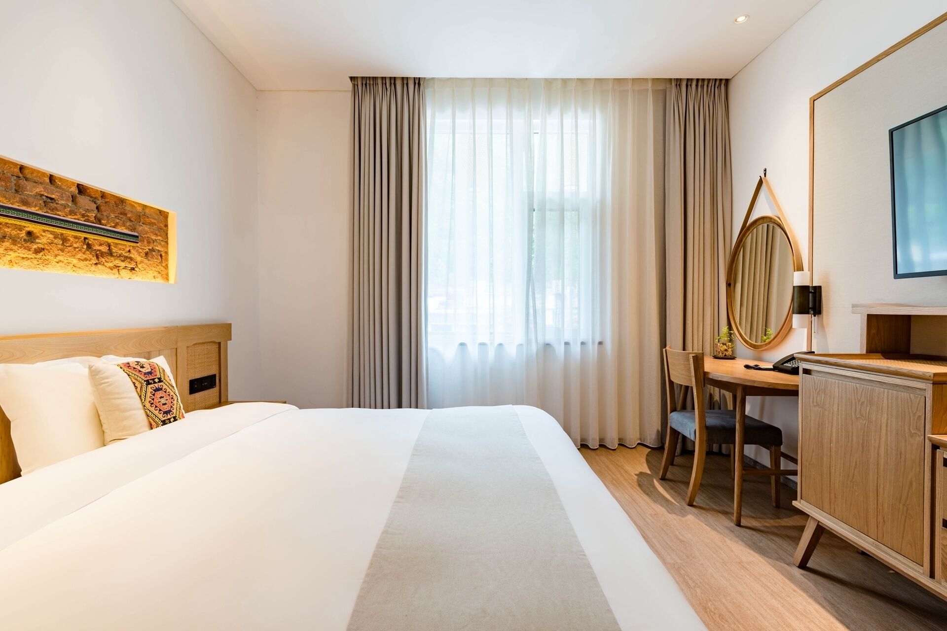 A hotel room with a large bed, a desk with a chair, a mirror, and a television.