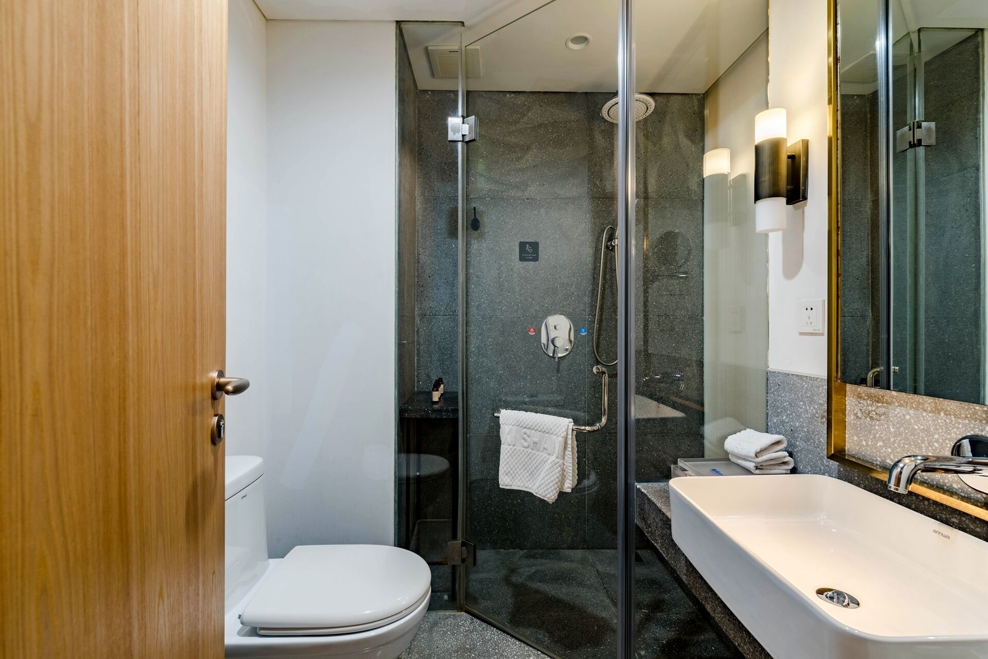 A modern bathroom with a glass-enclosed shower, a white toilet, and a large sink with a mirror.